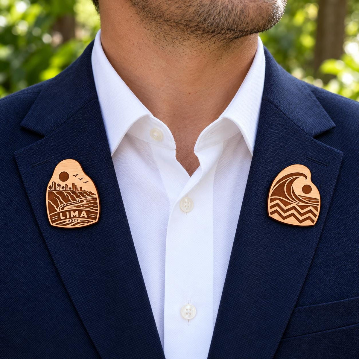 Two Lima engraved birch convention pin designs on the lapels of a navy man's suit outdoors.