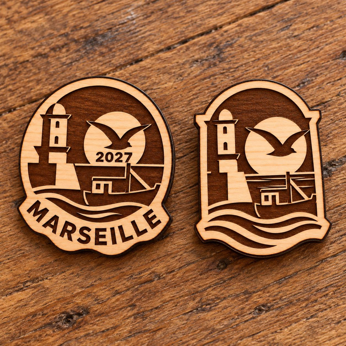 Two Marseille engraved birch convention pin designs lying face-up on a wooden table in natural light.