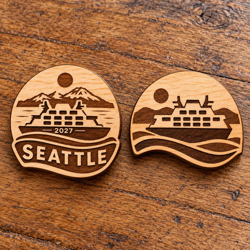 Two Seattle engraved birch convention pin designs lying face-up on a wooden table in natural light.