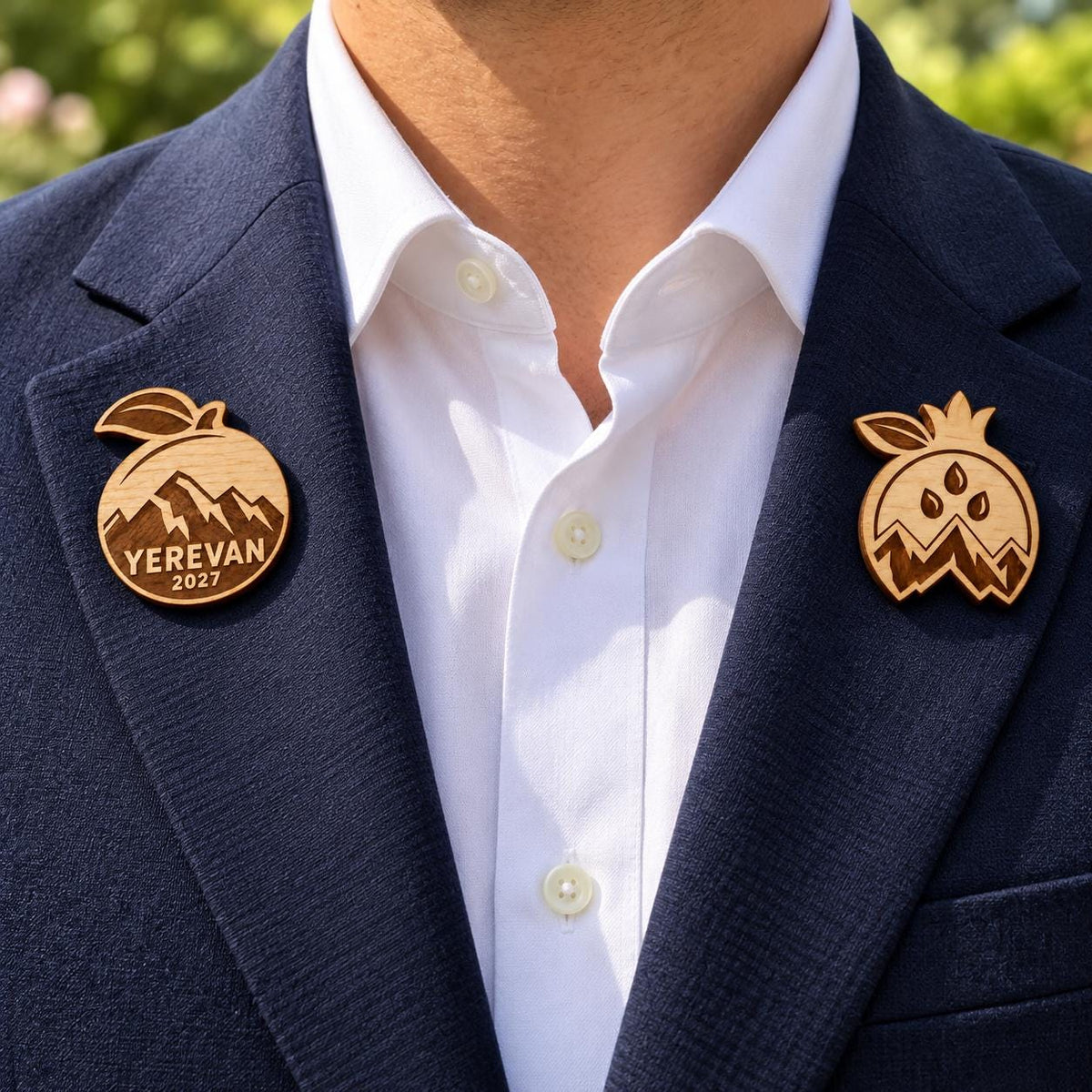 Two Yerevan engraved birch convention pin designs on the lapels of a navy man's suit outdoors.