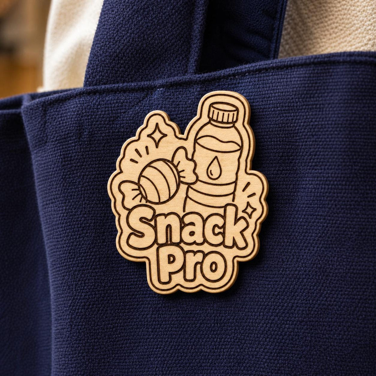 Close-up of the Convention Snack Pro natural birch engraved accessory attached to fabric, showing its dark artwork and shaped edge.