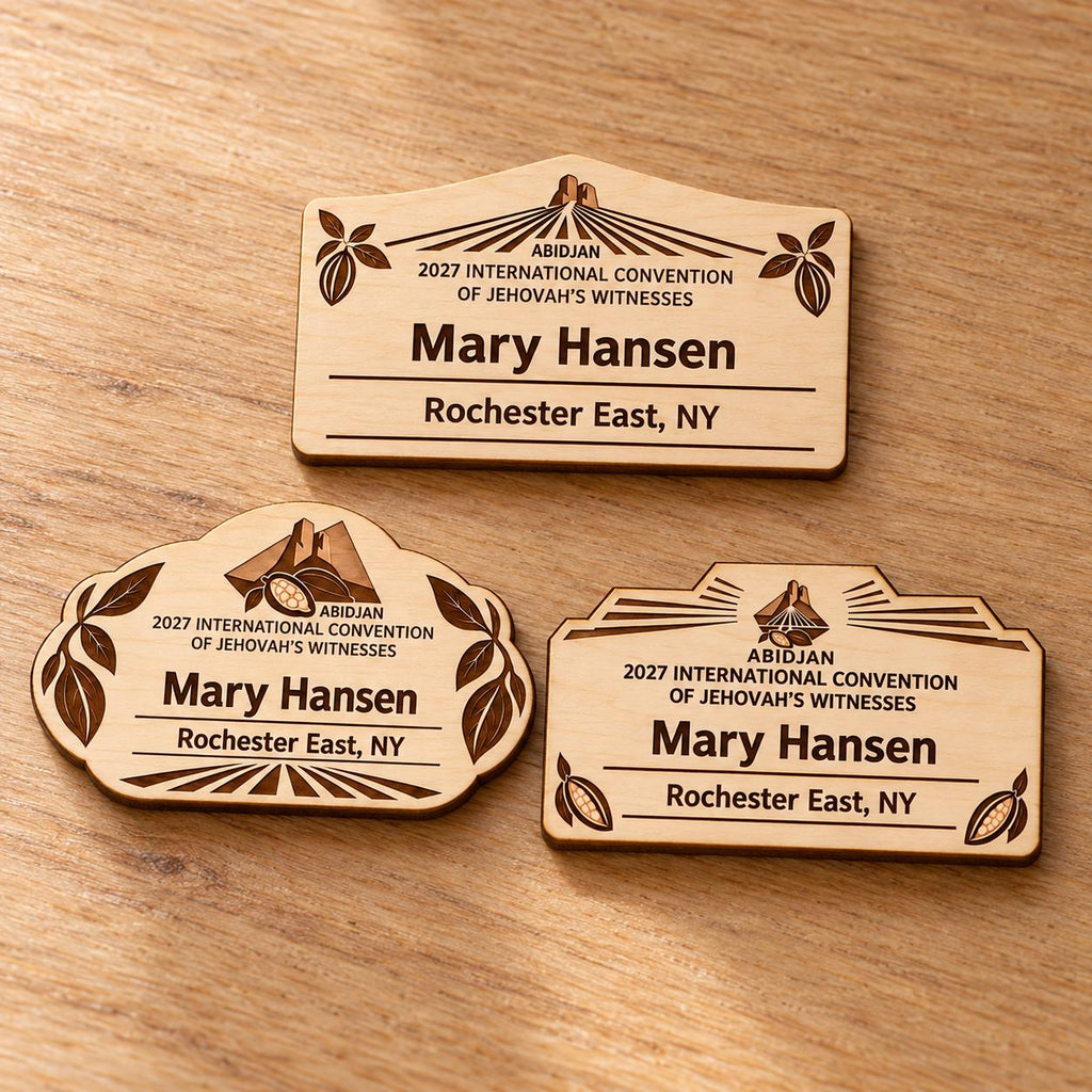 Three Abidjan mini natural-birch engraved badge designs, slot-free and laid separately on a light oak tabletop; each shows sample personalization.
