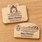 Two Lima mini natural-birch engraved badge designs, slot-free and laid separately on a light oak tabletop; each shows sample personalization.