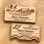 Two Strasbourg mini natural-birch engraved badge designs, slot-free and laid separately on a light oak tabletop; each shows sample personalization.