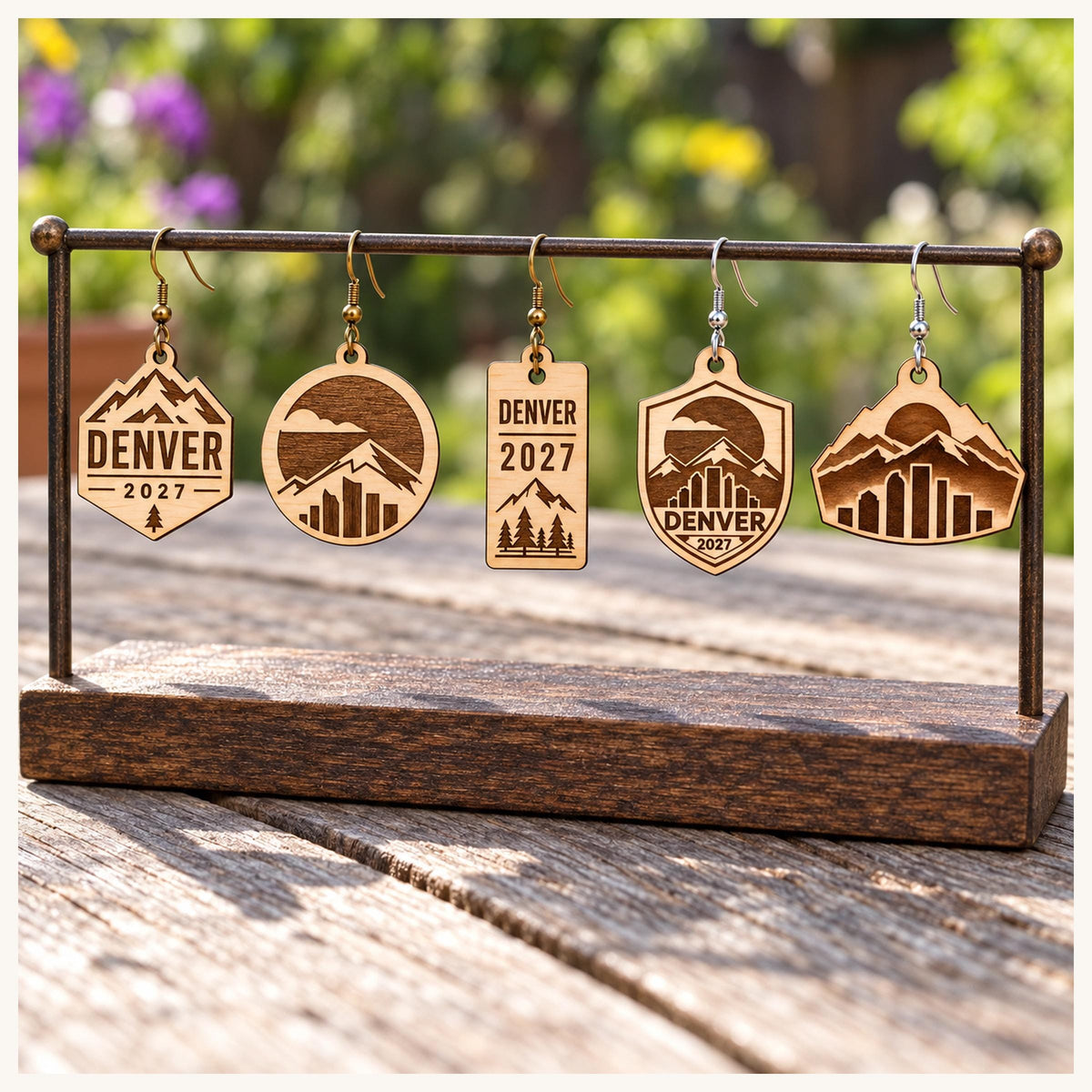 One earring from each selected Denver 2027 birch design on a wooden display stand outdoors.