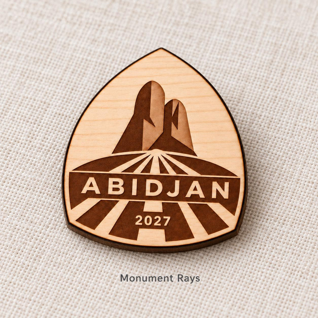 Close-up of Abidjan Monument Rays engraved birch pin on linen, with design name caption.
