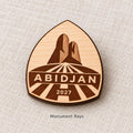 Close-up of Abidjan Monument Rays engraved birch pin on linen, with design name caption.