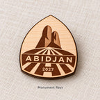 Close-up of Abidjan Monument Rays engraved birch pin on linen, with design name caption.