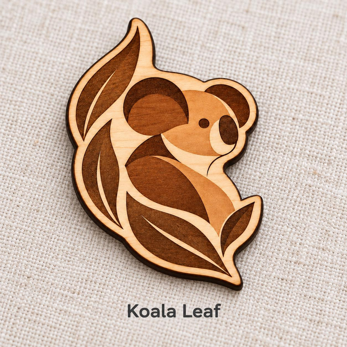 Close-up of Brisbane Koala Leaf engraved birch pin on linen, with design name caption.