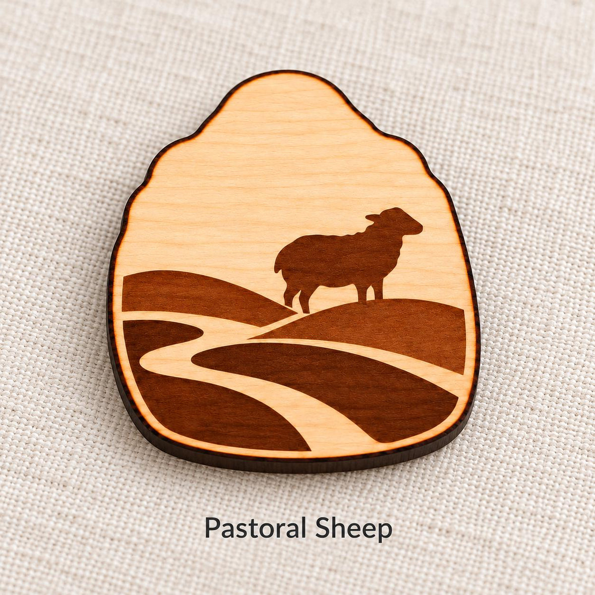 Close-up of Cardiff Pastoral Sheep engraved birch pin on linen, with design name caption.