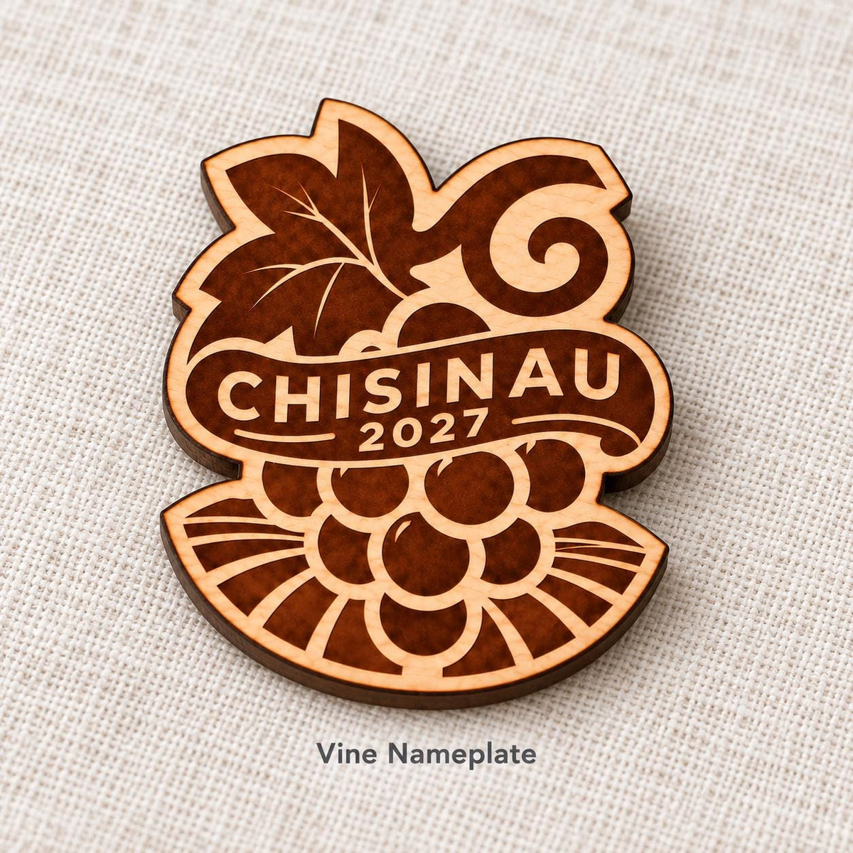 Close-up of Chișinău Vine Nameplate engraved birch pin on linen, with design name caption.