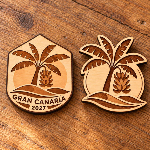 Two Gran Canaria engraved birch convention pin designs lying face-up on a wooden table in natural light.
