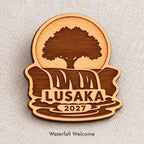 Close-up of Lusaka Waterfall Welcome engraved birch pin on linen, with design name caption.
