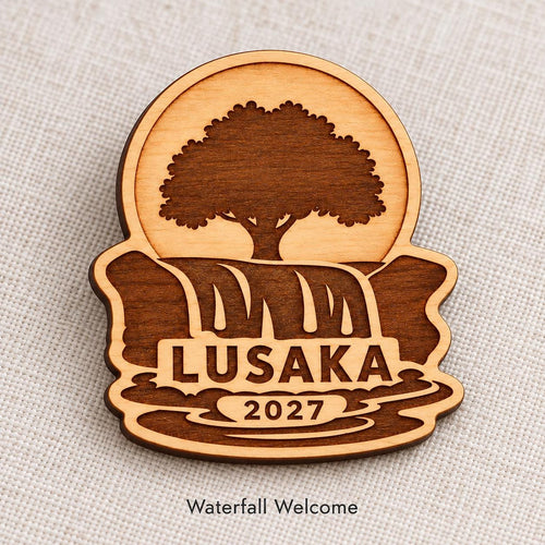 Close-up of Lusaka Waterfall Welcome engraved birch pin on linen, with design name caption.