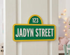 Green and yellow personalized street-style sign reading Jadyn Street and 123 on a white bedroom door.
